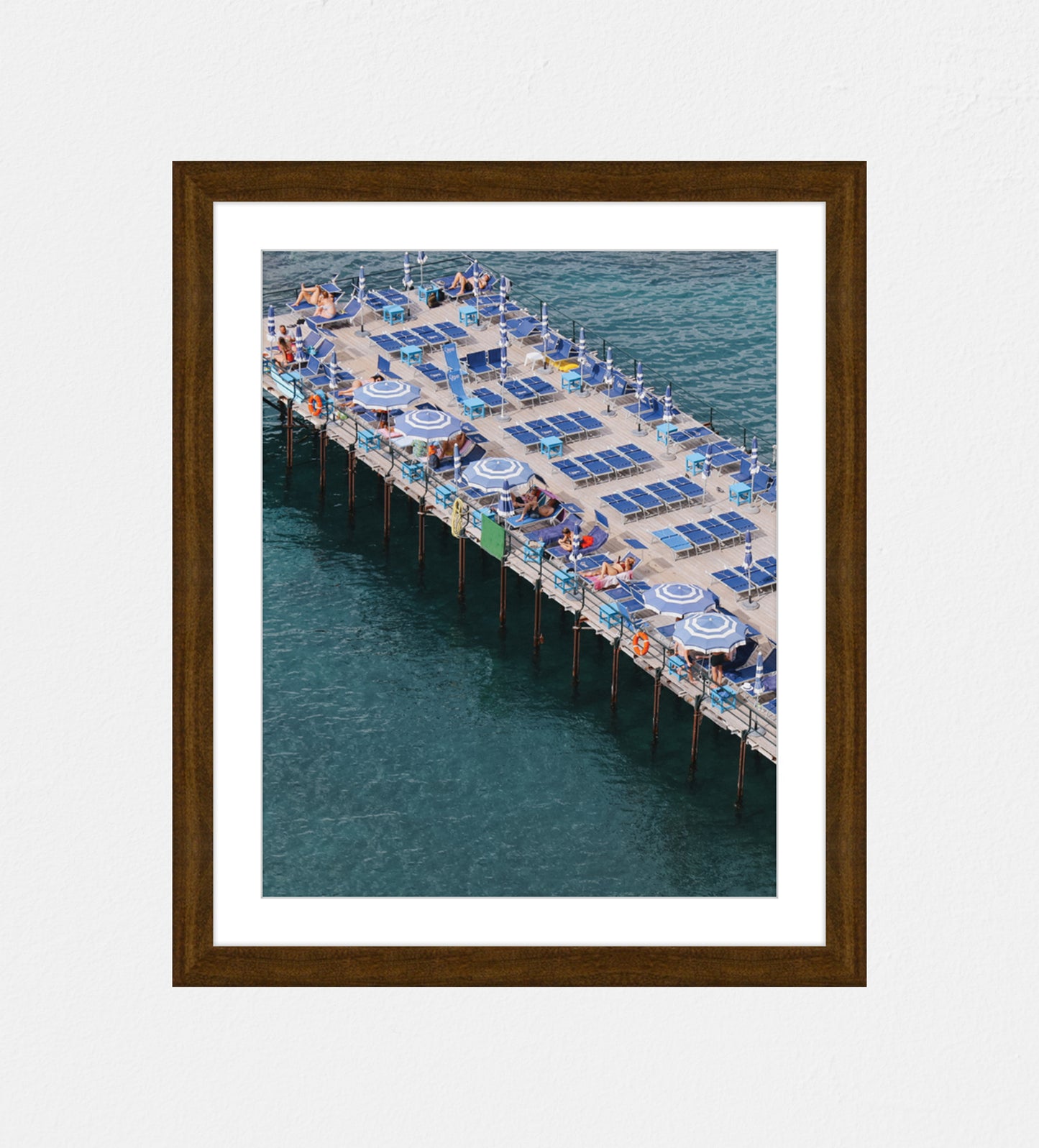 Photo of a pier at an angled shot in Sorrento, Italy. Featuring blue sunbeds and blue and white umbrellas.