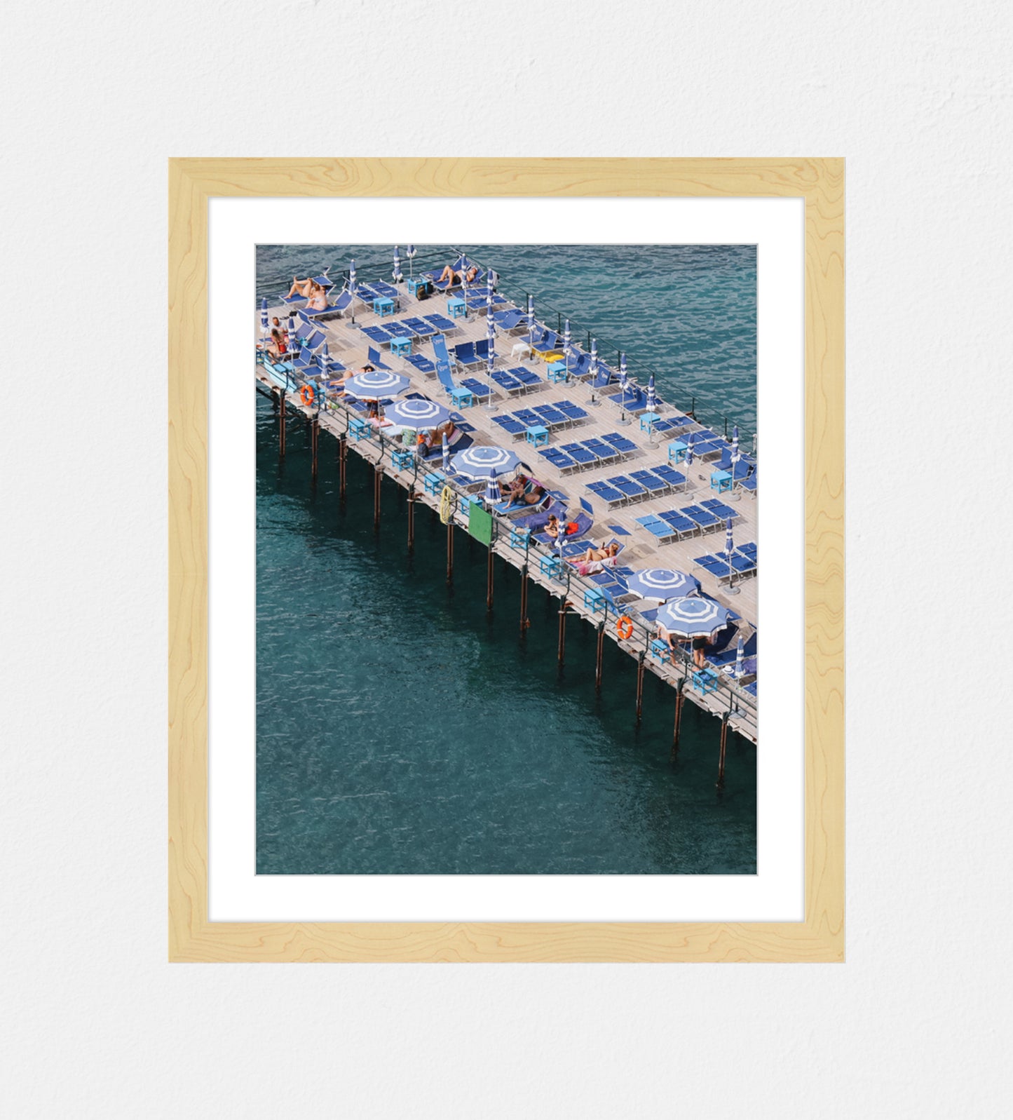 Photo of a pier at an angled shot in Sorrento, Italy. Featuring blue sunbeds and blue and white umbrellas.