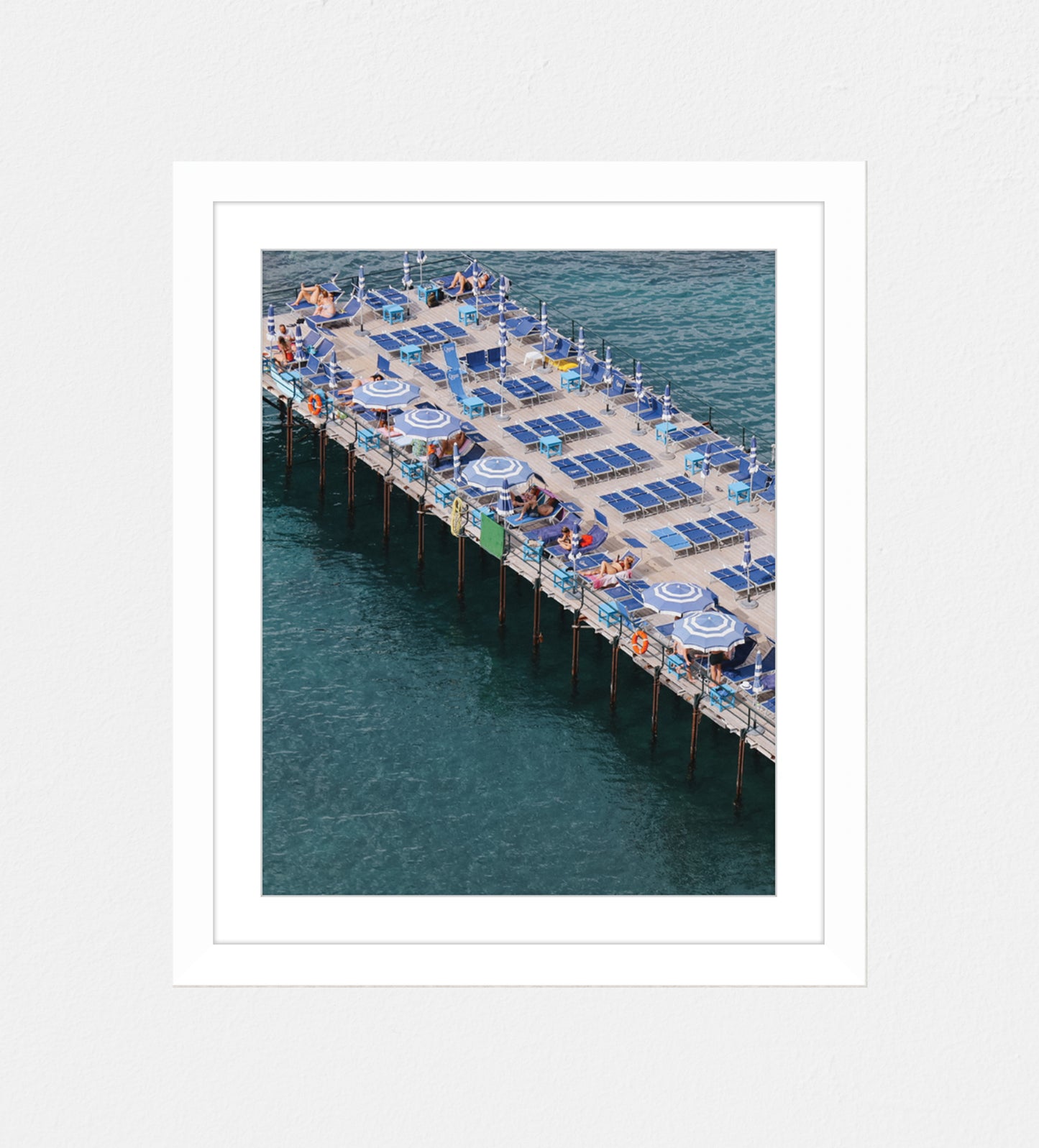 Photo of a pier at an angled shot in Sorrento, Italy. Featuring blue sunbeds and blue and white umbrellas.